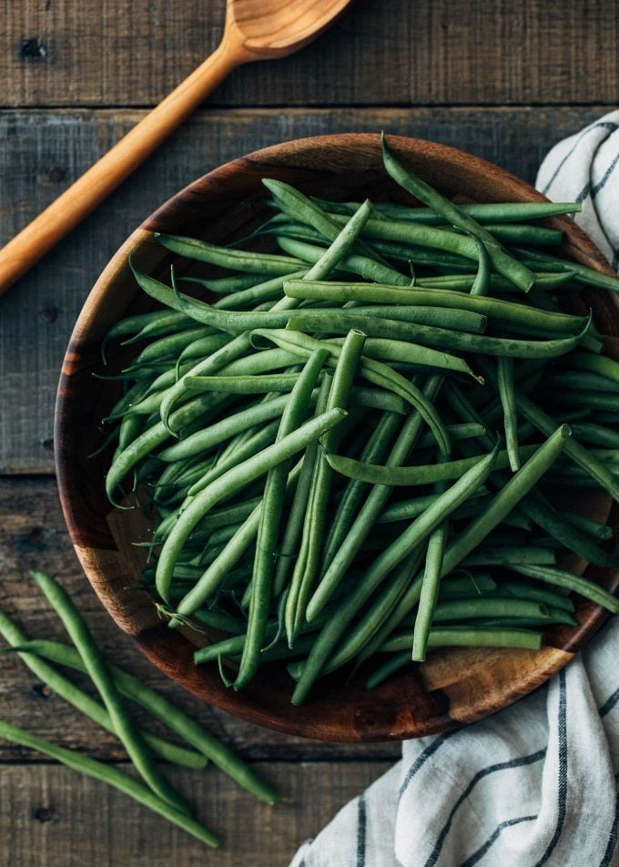 uncooked haricots verts in a wood bowl on a rustic wood board