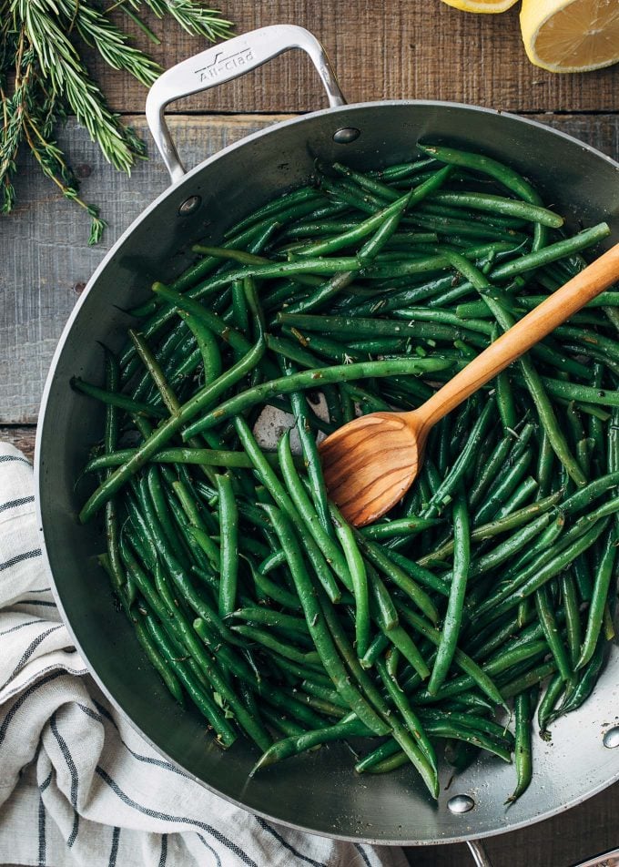 haricots verts in an all clad pan with brown butter and a wooden spoon