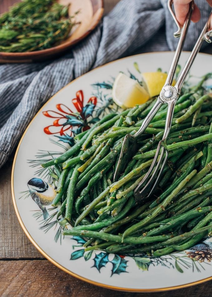 brown butter green beans being served with silver serving tongs from a Christmas platter