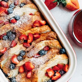 overnight croissant baked french toast with strawberries and blueberries in a stub casserole dish