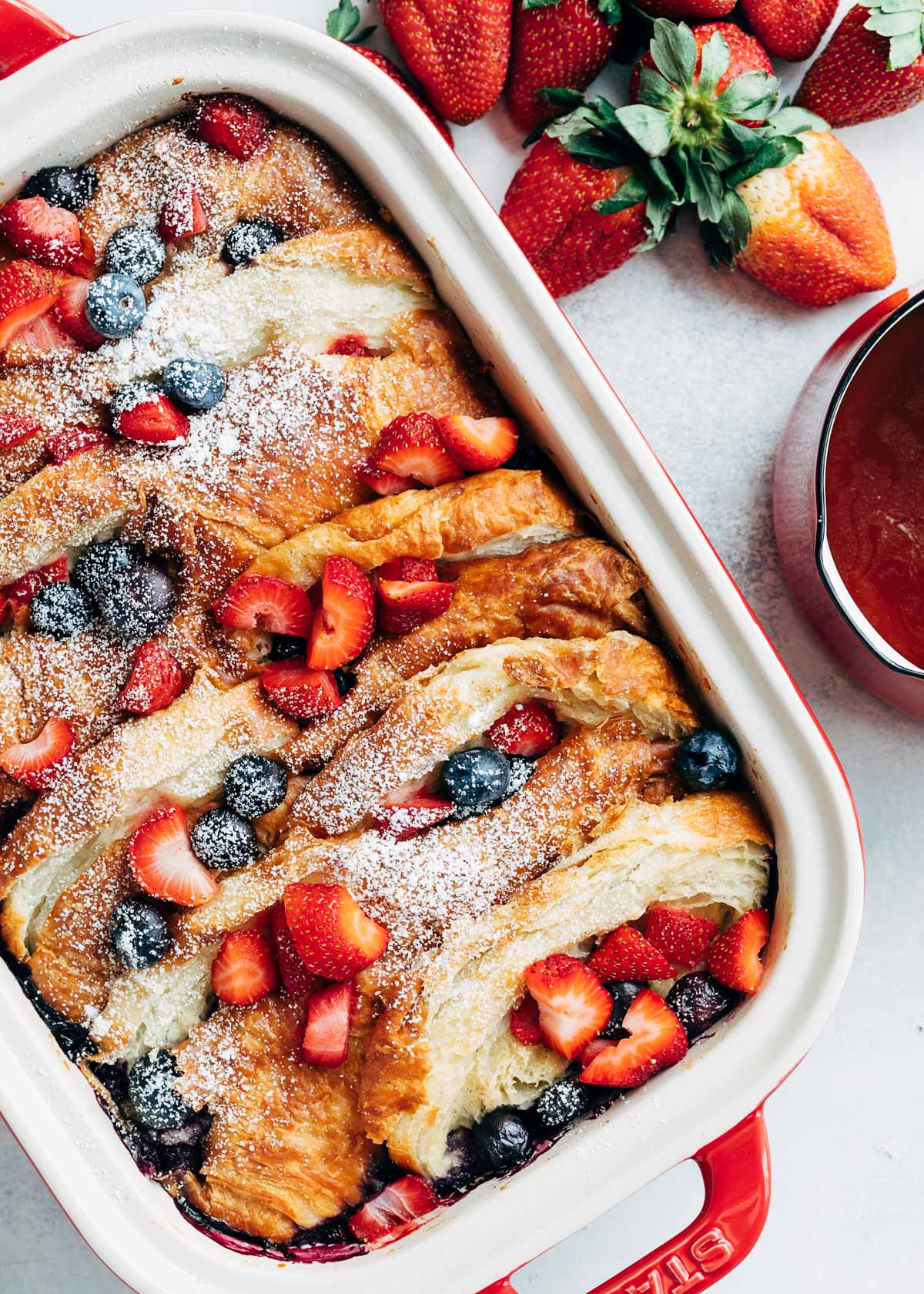 overhead of a croissant french toast bake with berries in a staub rectangular baker