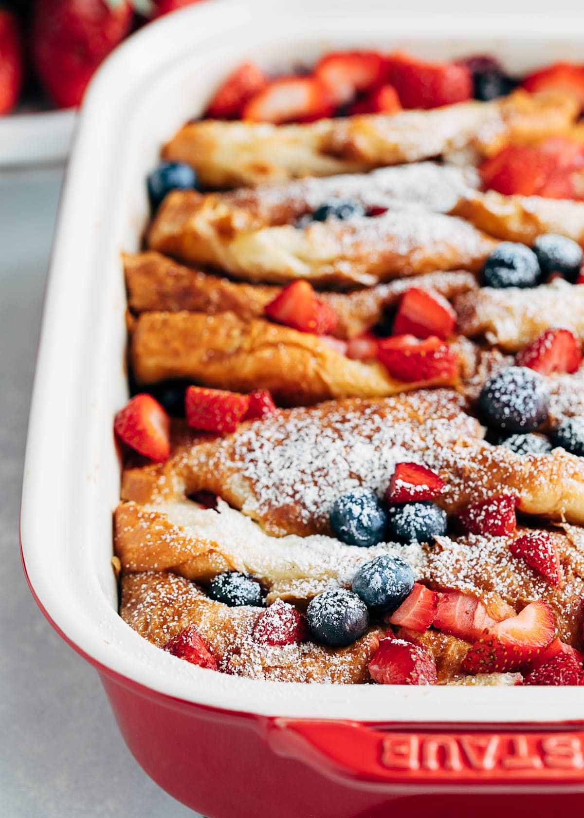 side view of a baked french toast casserole in a baking dish, dusted with powdered sugar