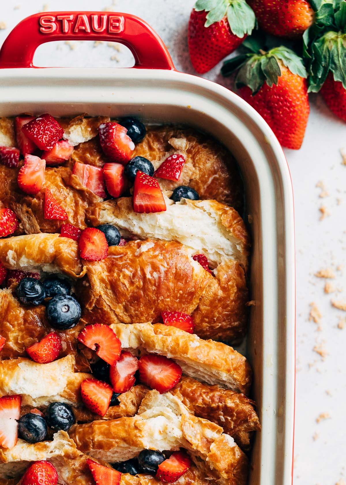 closeup overhead photo of an unbaked croissant french toast casserole with berries in a rectangular baking dish