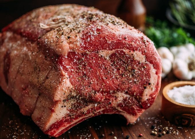 sliced prime rib on a wood carving board with carving knife and fork