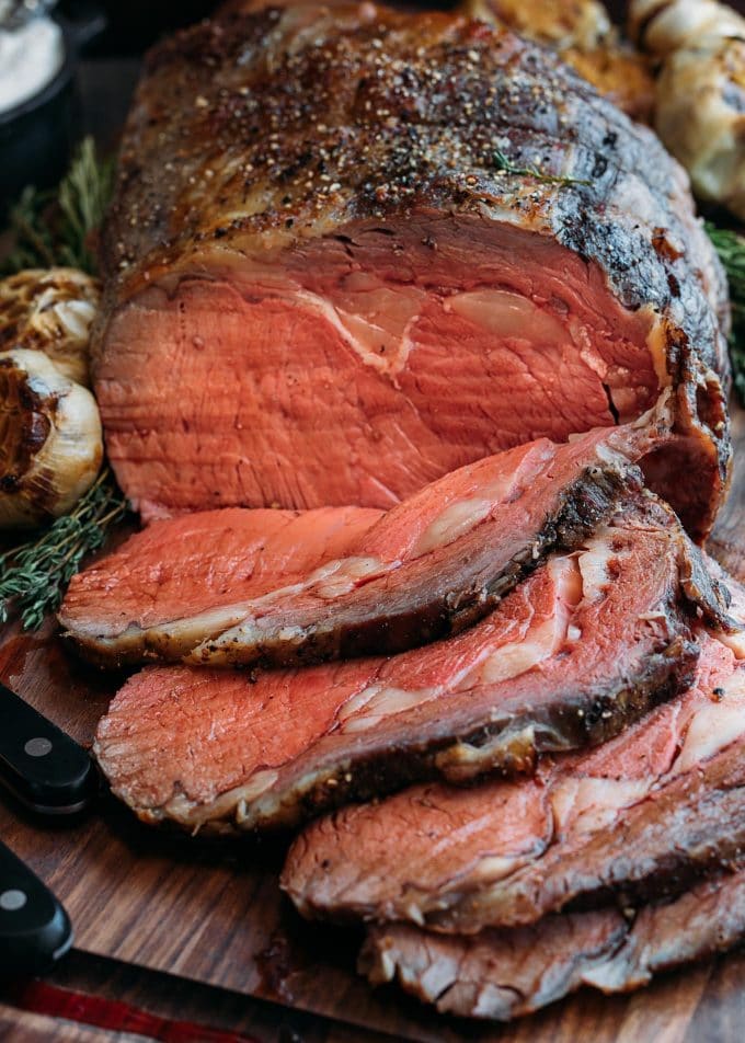 sliced prime rib on a wood carving board with carving knife and fork