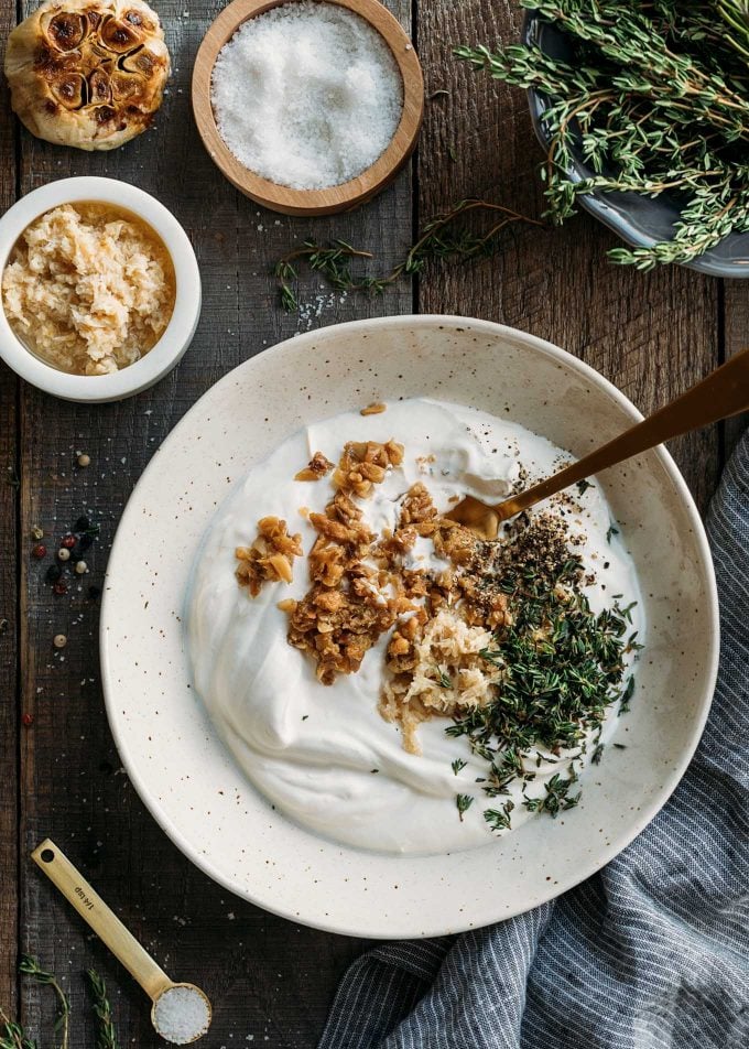 sour cream in a ceramic bowl with a spoon and roasted garlic, thyme, and horseradish