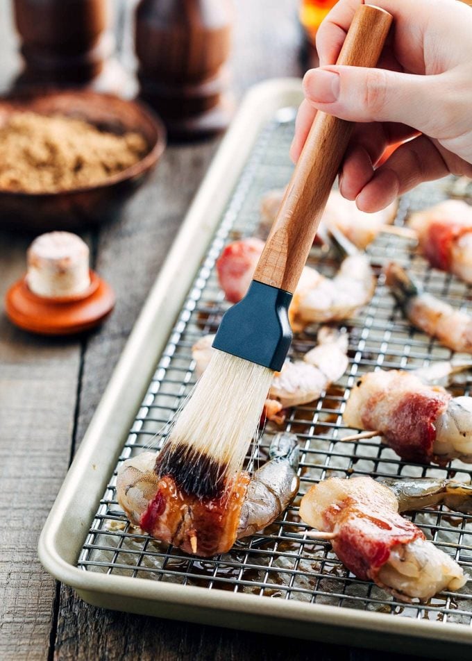 brushing brown sugar bourbon glaze onto bacon-wrapped shrimp