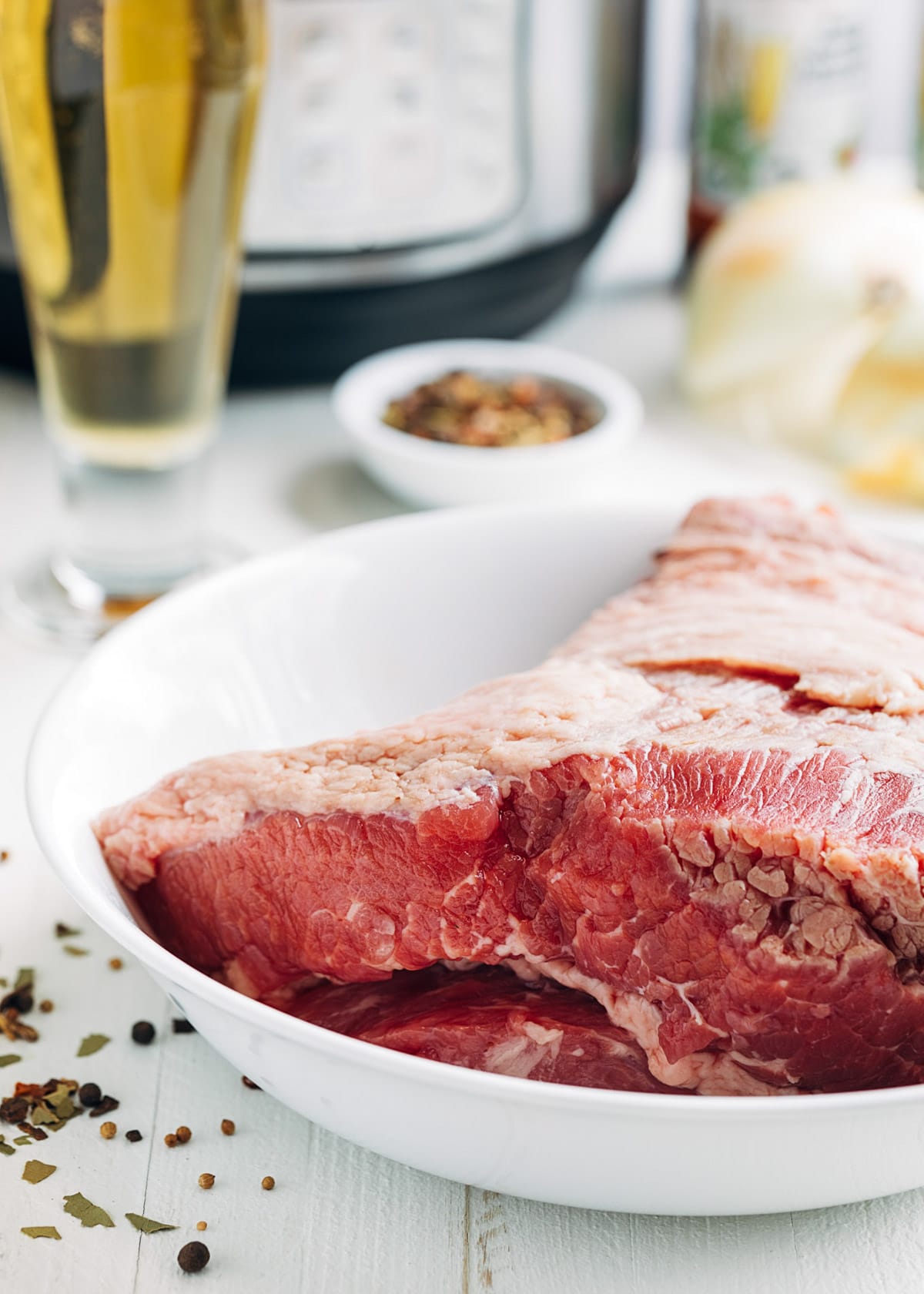 uncooked corned beef in a white bowl with a glass of beer and an instant pot in the background