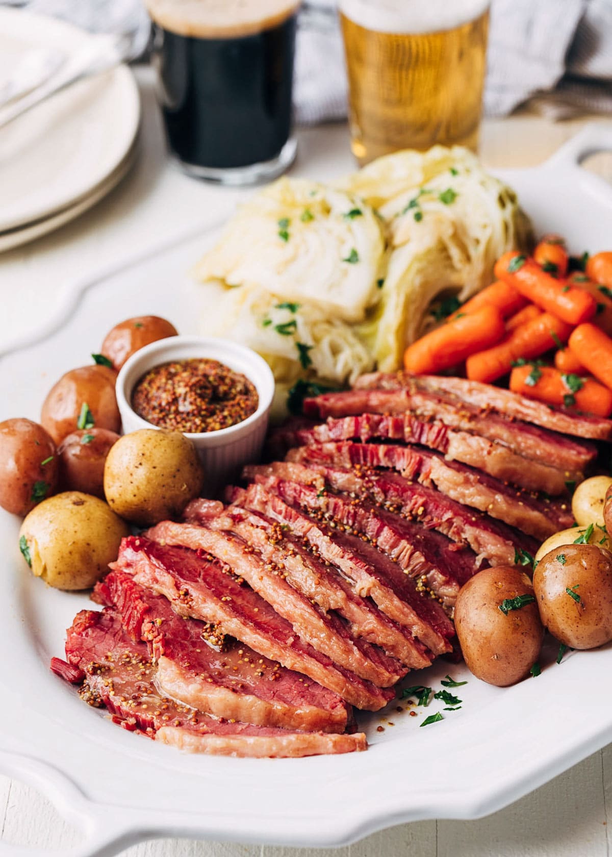 slices of instant pot corned beeef on a white platter with baby potatoes, carrots, and cabbage wedges