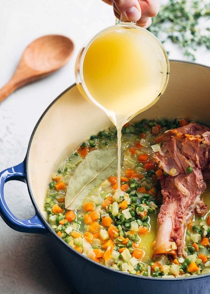 pouring chicken stock into a pot of split pea soup with a ham bone