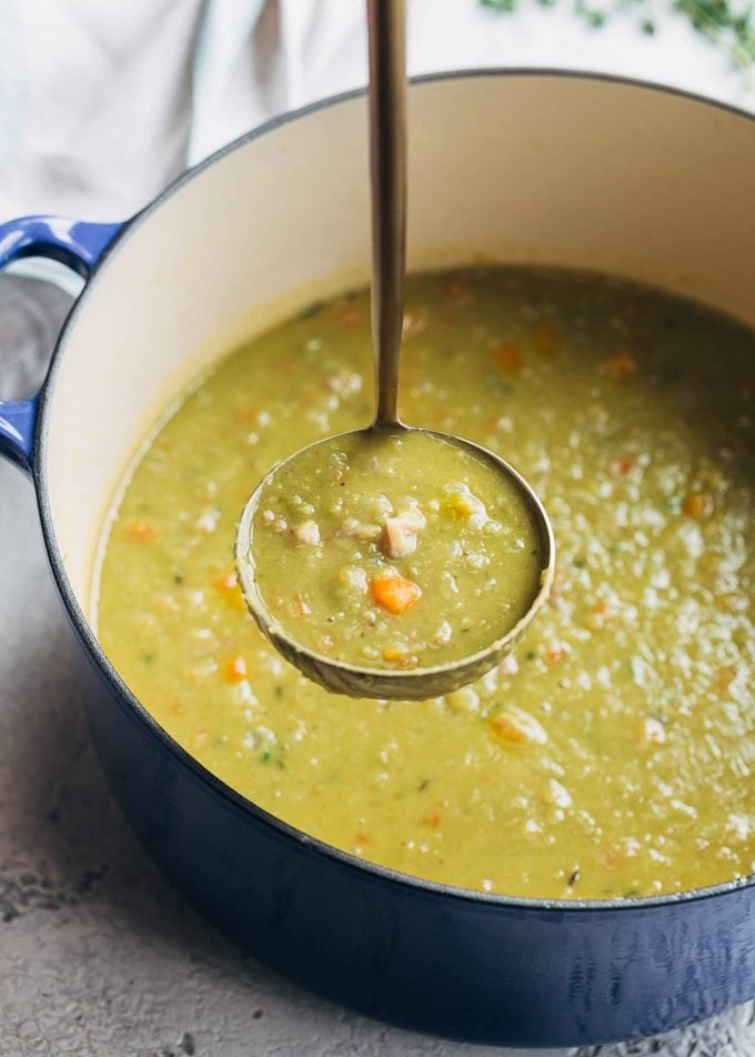 ladleful of split pea soup and ham in a blue cast iron pot