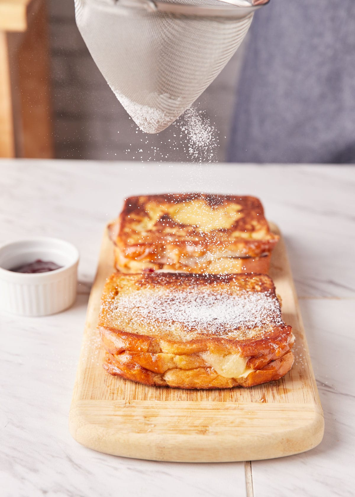 dusting powdered sugar onto a pan fried monte cristo sandwich on a wood board