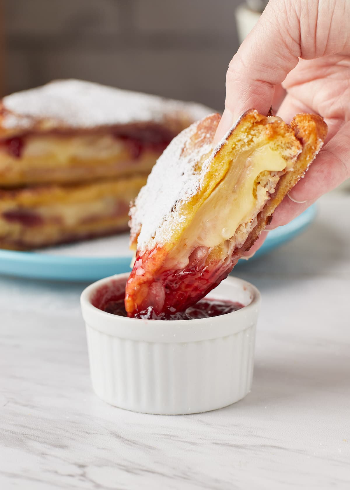 dipping half of a monte cristo sandwich into a bowl of jelly