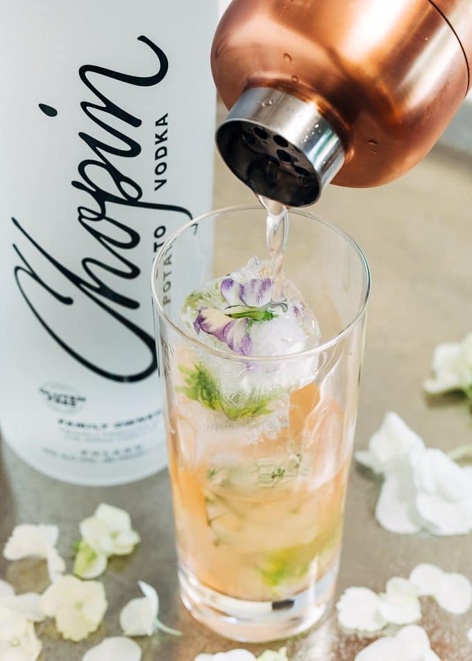 pouring vodka cocktail into a glass with flower ice cubes