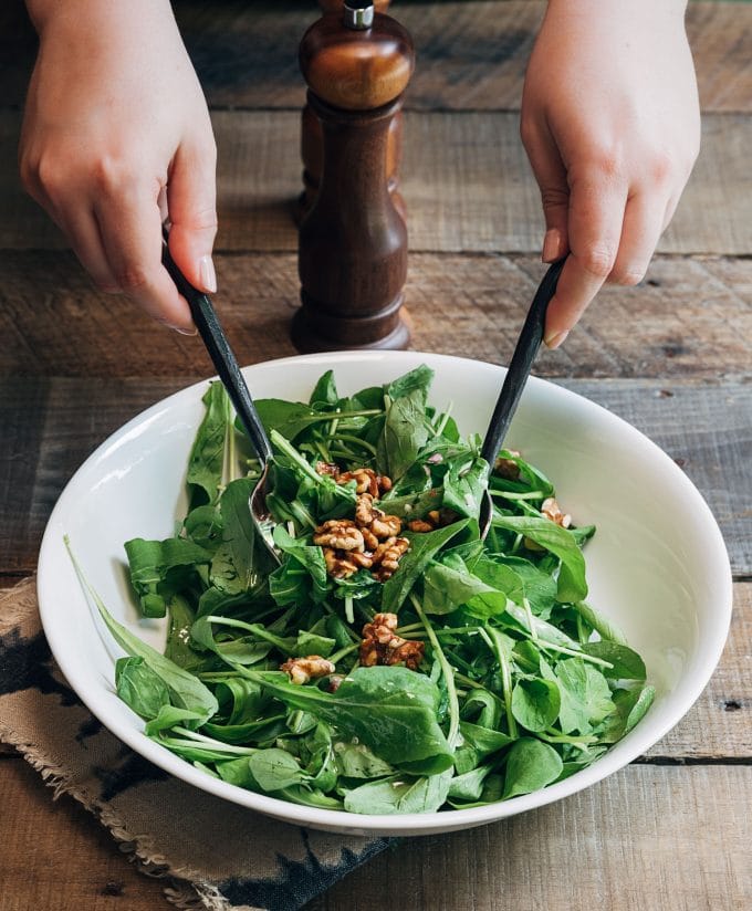 tossing baby rucula and walnuts with vinaigrette