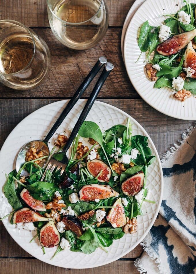 fig salad with baby arugula on ivory plates with glasses of white wine