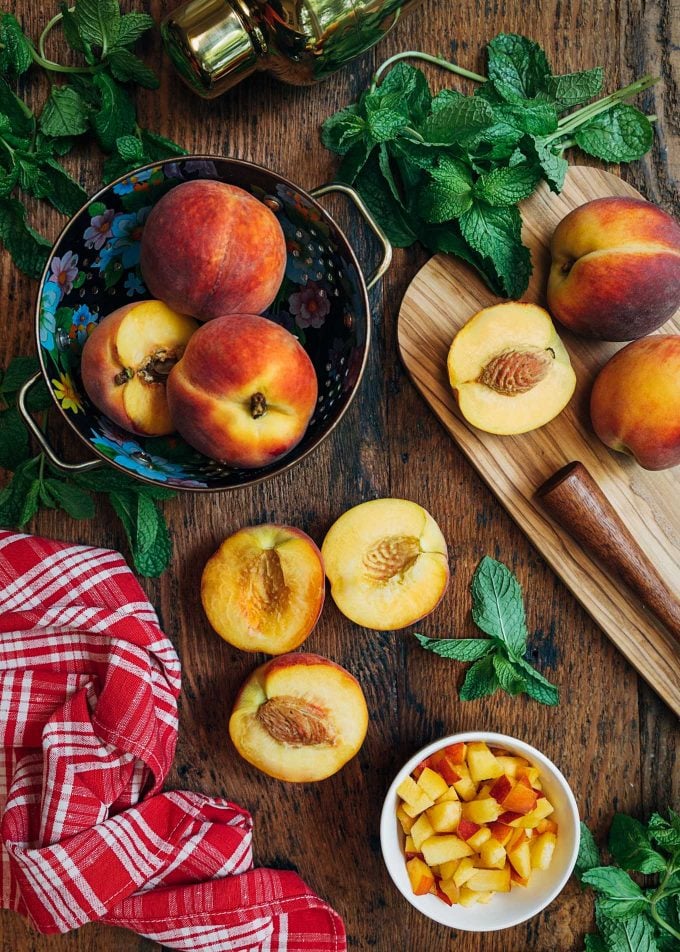 whole and cut peaches on a board with mint leaves