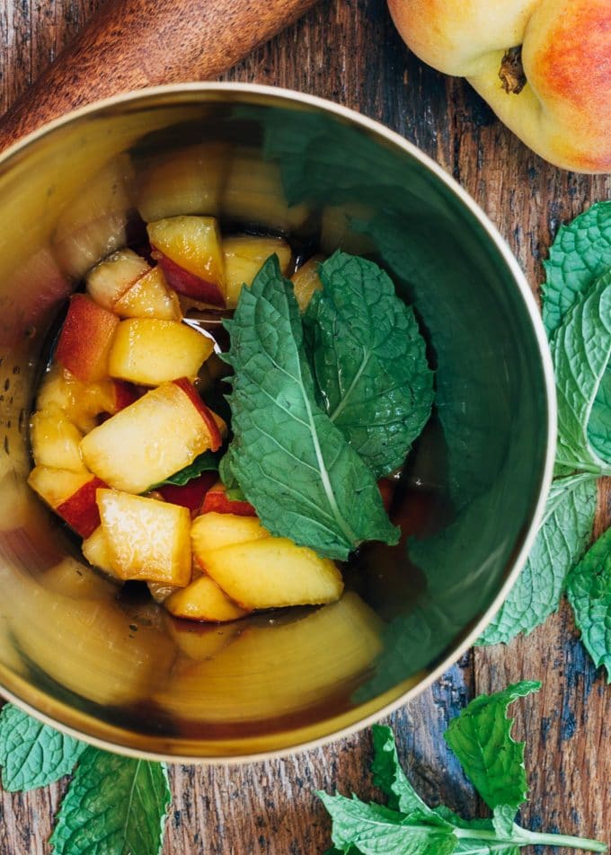 peaches and mint leaves in a cocktail shaker for a bourbon smash cocktail