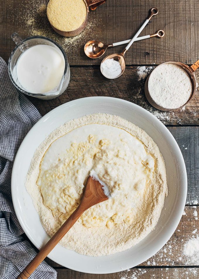 adding buttermilk to cornbread biscuit dough in a bowl