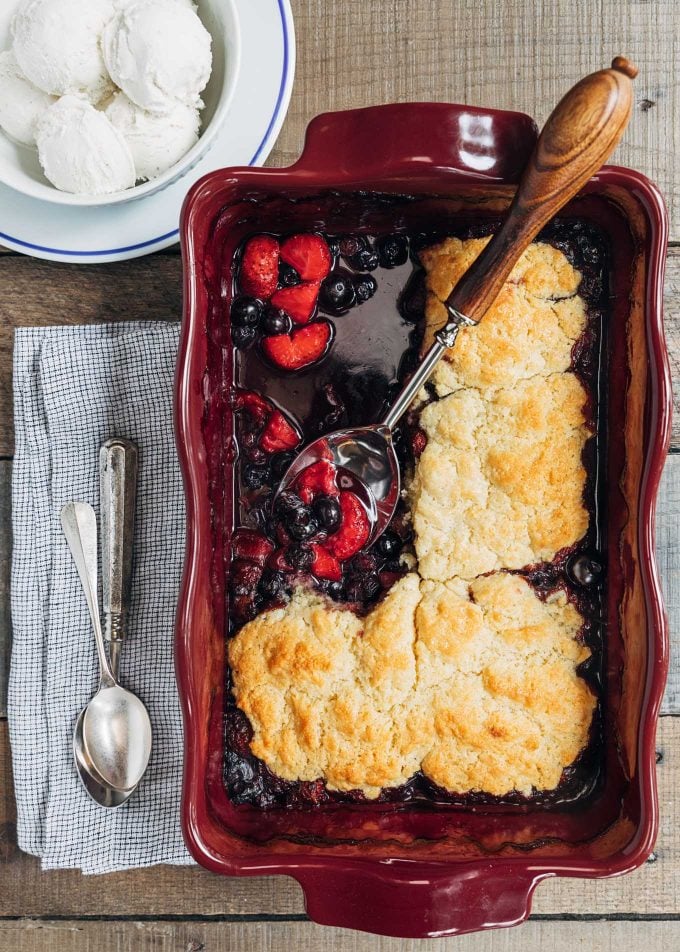 mixed berry cobbler in an emile henry baking dish with a bowl of ice cream