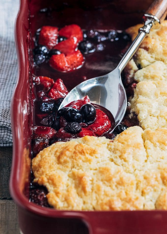 mixed berry cobbler in a baking dish with a spoon