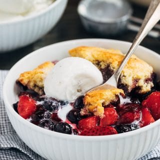 mixed berry cobbler with cornbread biscuit topping and vanilla ice cream in a bowl