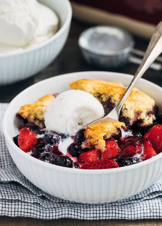 mixed berry cobbler with cornbread biscuit topping and vanilla ice cream in a bowl
