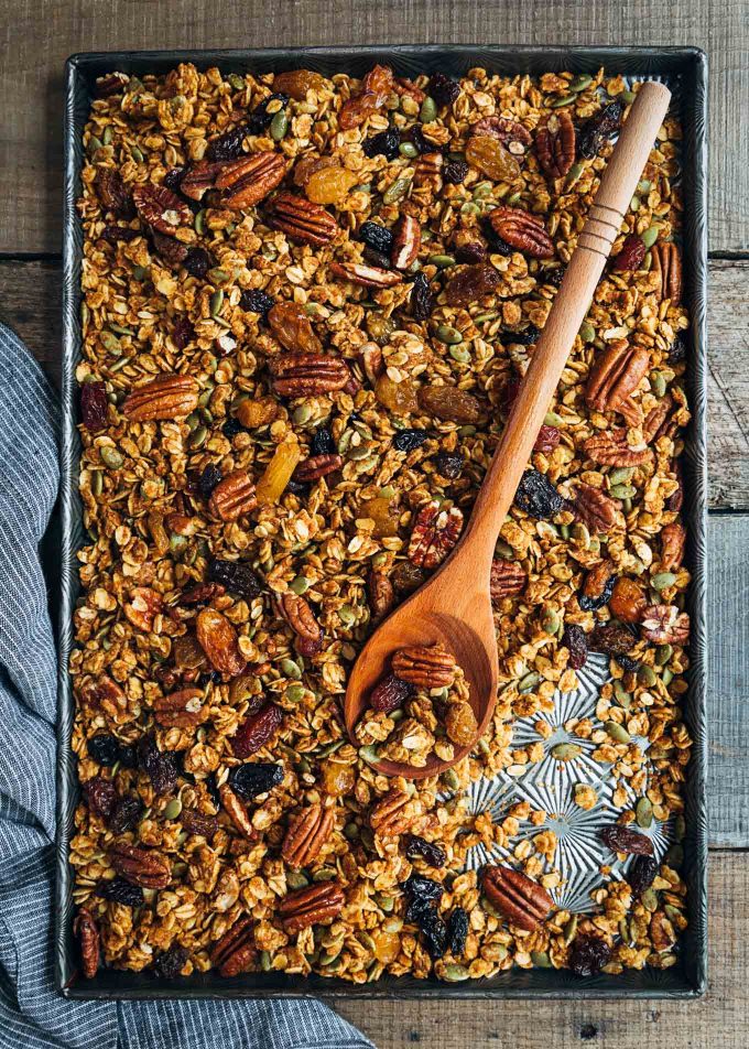 baked pumpkin granola on a sheet pan with a wooden spoon