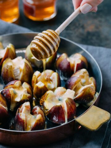 drizzling honey over baked Cambozola stuffed figs with a honey dipper