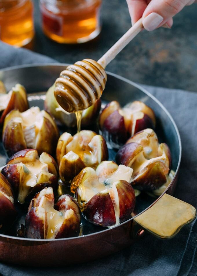 drizzling honey over baked Cambozola stuffed figs with a honey dipper