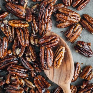 caramelized pecans on a baking sheet with a wooden spoon