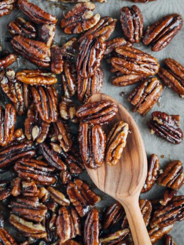 caramelized pecans on a baking sheet with a wooden spoon