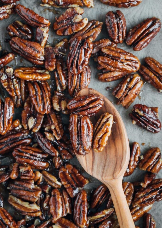 caramelized pecans on a baking sheet with a wooden spoon