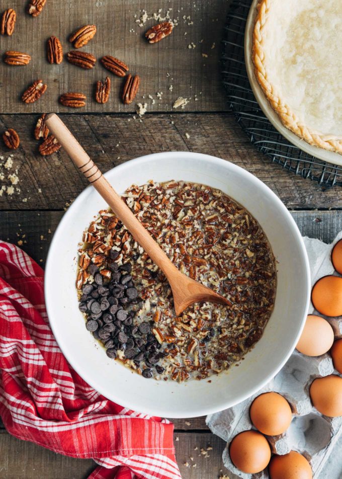 ingredients for chocolate pecan pie with bourbon in a white bowl with a wooden spoon