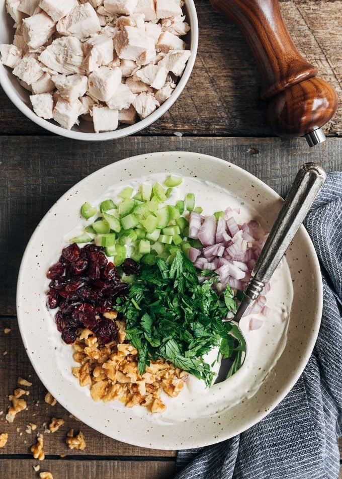 dried cranberries, celery, shallots, parsley, and walnuts in a bowl of chicken salad dressing