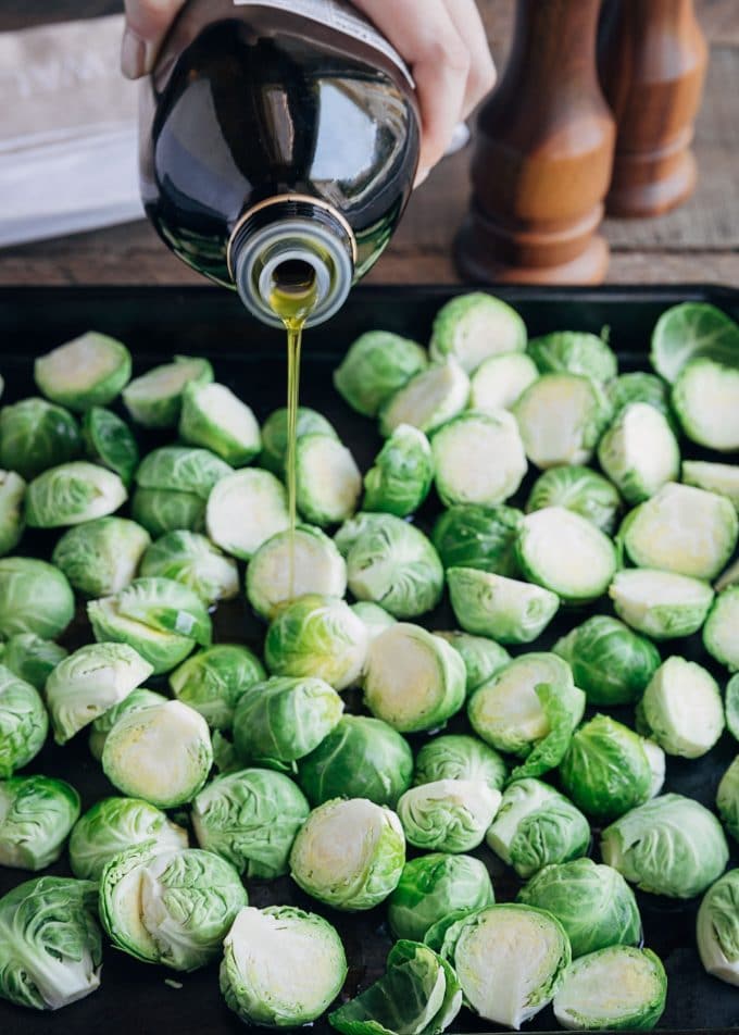 pouring olive oil over halved brussels sprouts on a baking pan