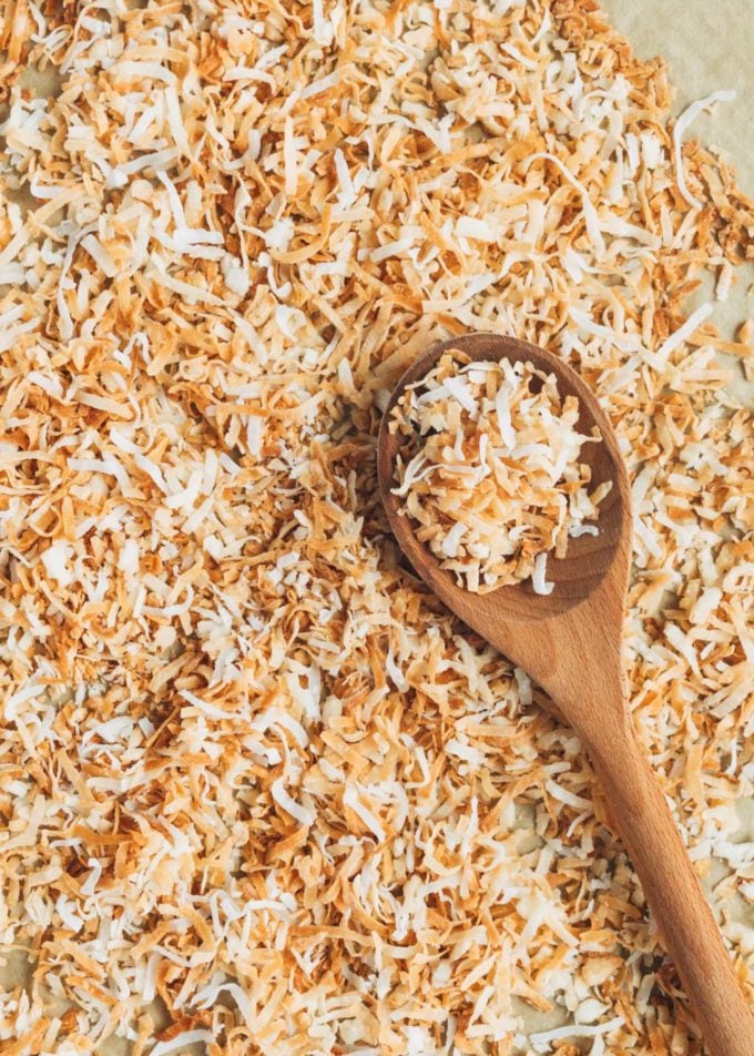 toasted coconut flakes on a sheet pan with a wooden spoon