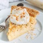 slice of coconut custard pie on a plate with whipped cream and toasted coconut flakes