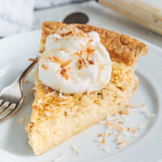 slice of coconut custard pie on a plate with whipped cream and toasted coconut flakes