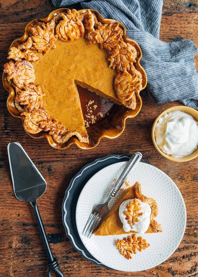 slice of pumpkin pie on a plate and a whole pie with a slice missing