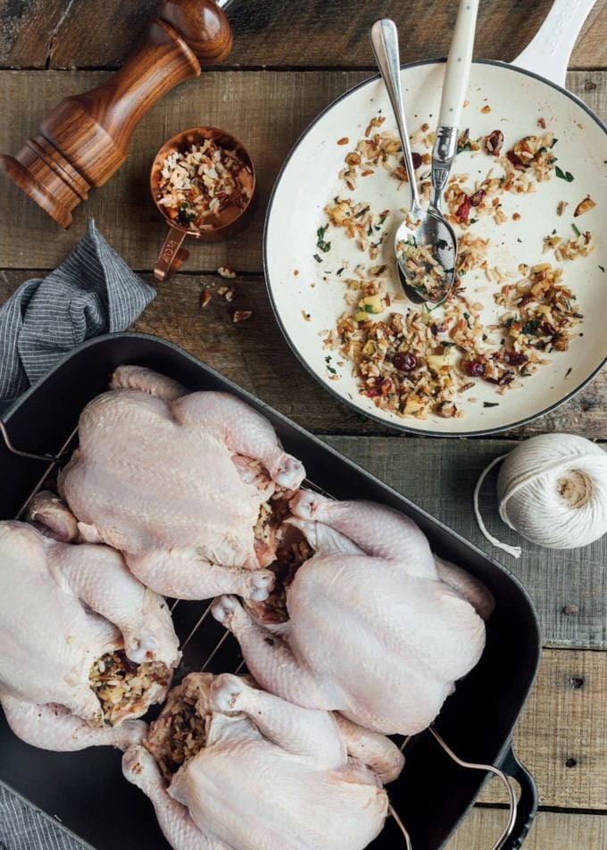 stuffed cornish game hens in a roasting pan with a pan of rice stuffing