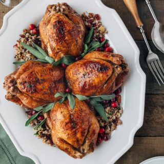 stuffed cornish hens on a white platter with fresh sage