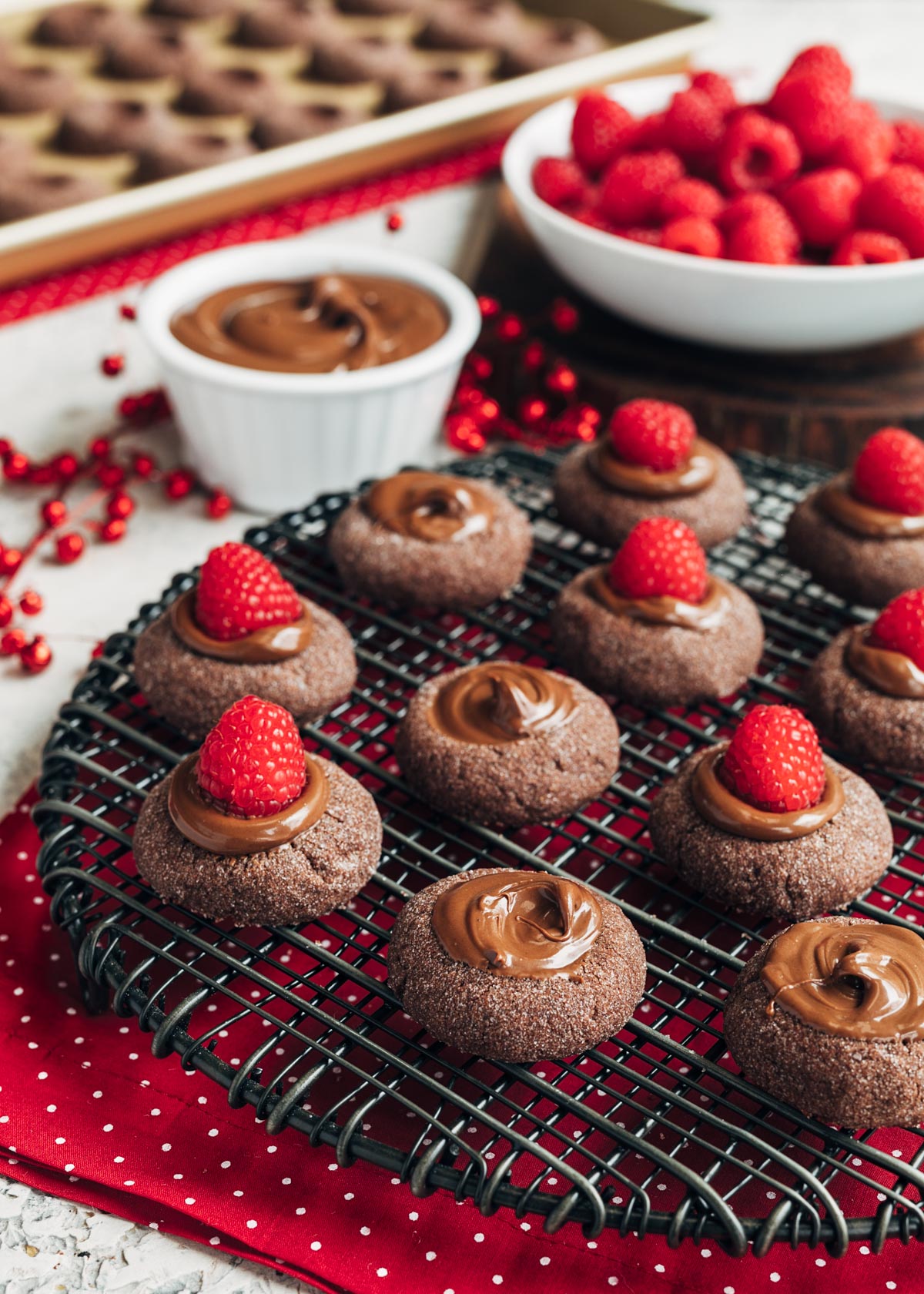 chocolate hazelnut thumbprint cookies on a black wire rack, some topped with raspberries