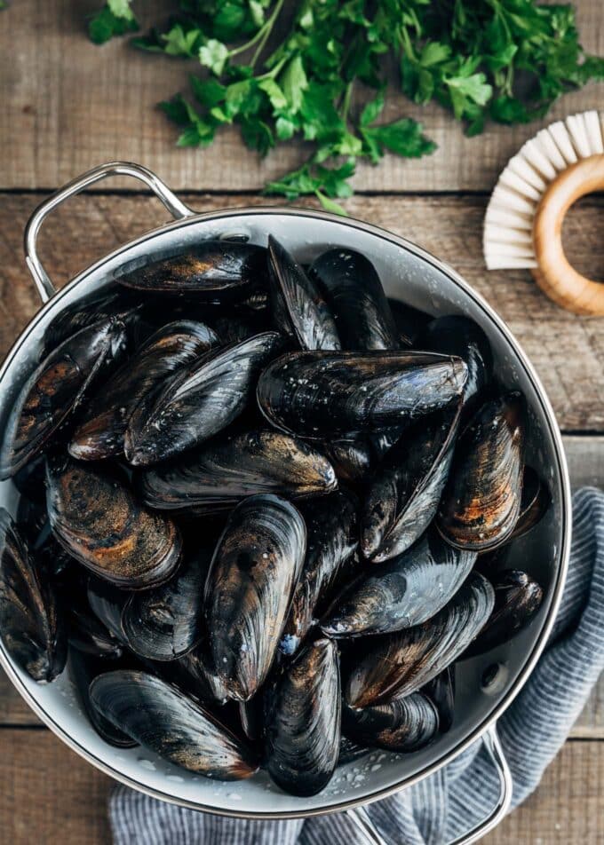 cleaned uncooked mussels in a colander with a brush on the board