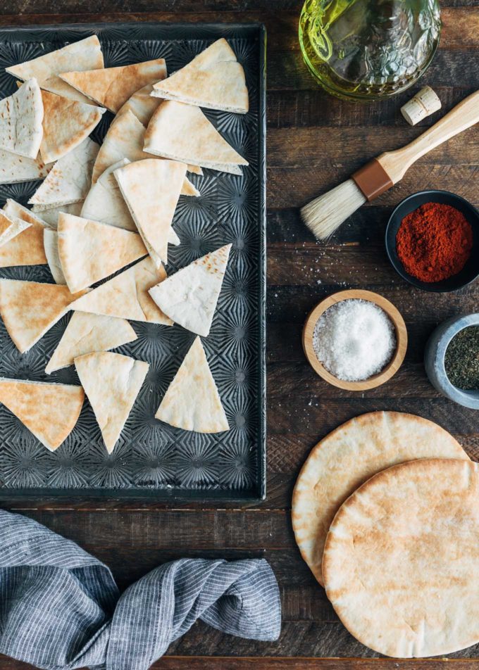 cut pita wedges on a baking sheet and bowls of seasonings for pita chips