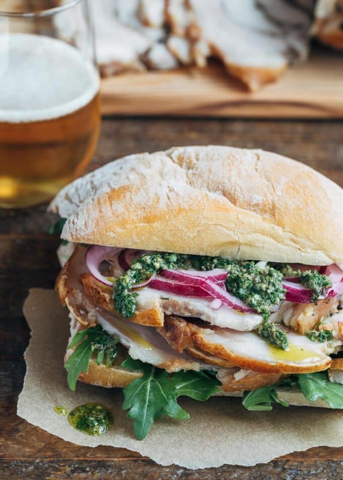 porchetta sandwich with salsa verde and pickled onions on a ciabatta roll