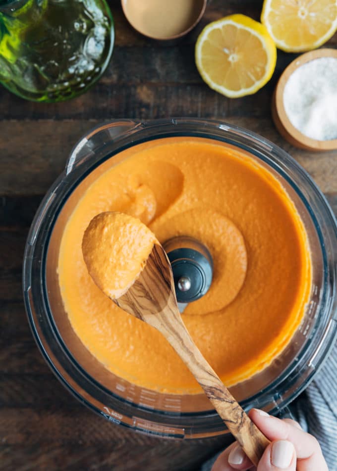 spoonful of roasted red pepper hummus held over a food processor bowl