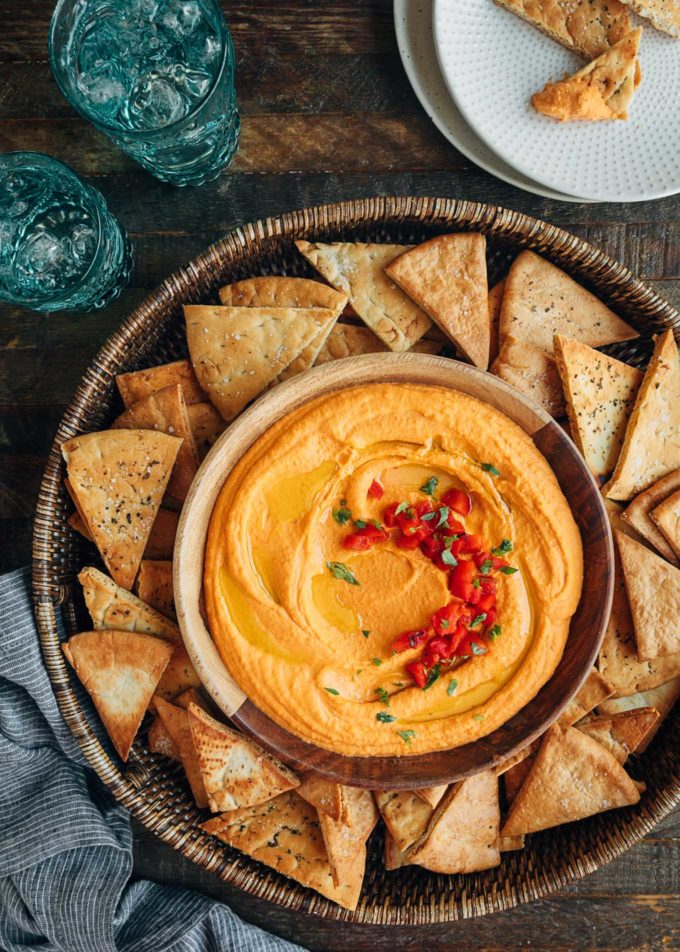 round serving platter of roasted red pepper hummus with pita chips