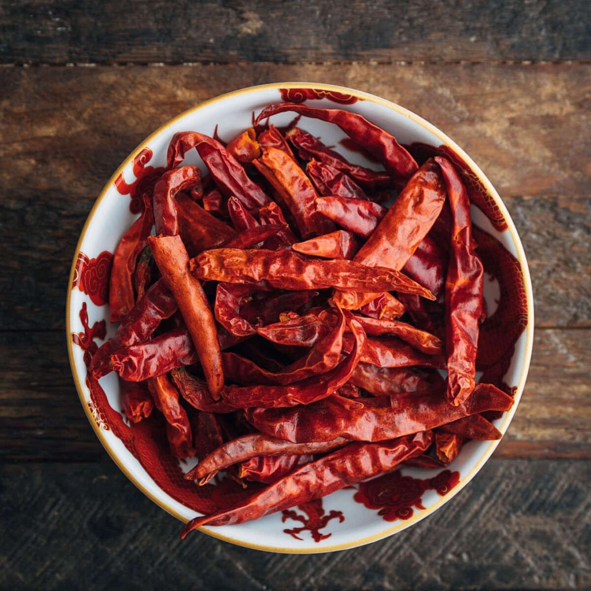 dried red chiles in a bowl on a wood board