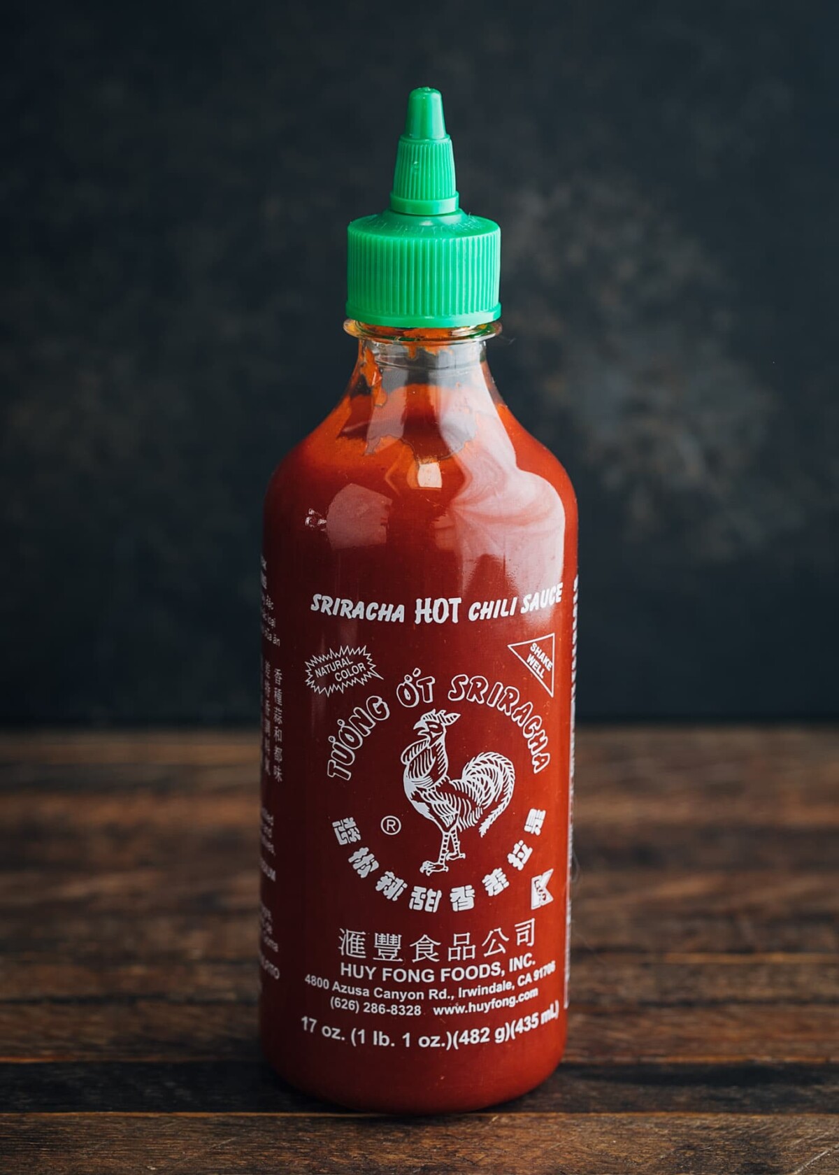 bottle of Huy Fong Foods sriracha on a wood board with a black background